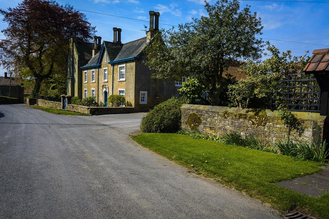 A quiet village road curving past stone houses and a garden wall