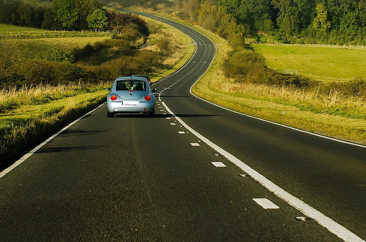 A small car on a winding two-lane road through green fields